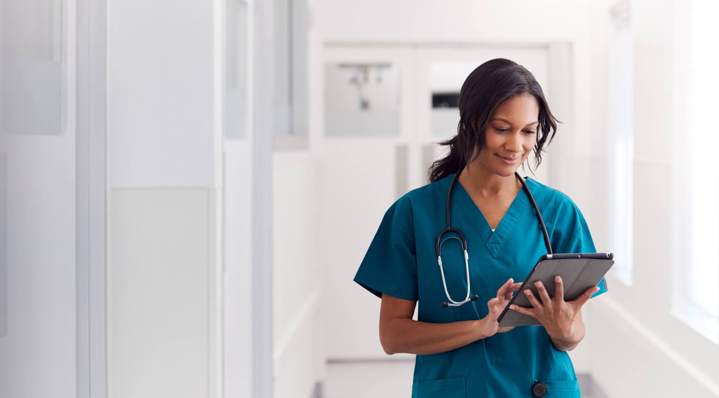 Female doctor wearing scrubs in hospital corridor using digital tablet