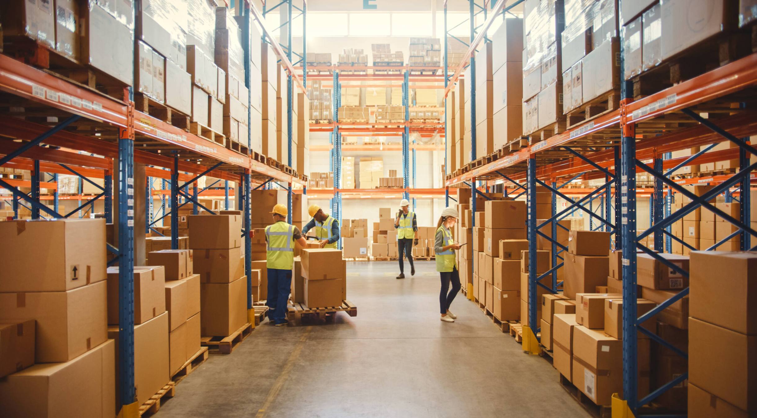 Retail warehouse full of shelves with goods in cardboard boxes, workers scan and sort packages, move inventory with pallet trucks and forklifts. Product distribution delivery center.